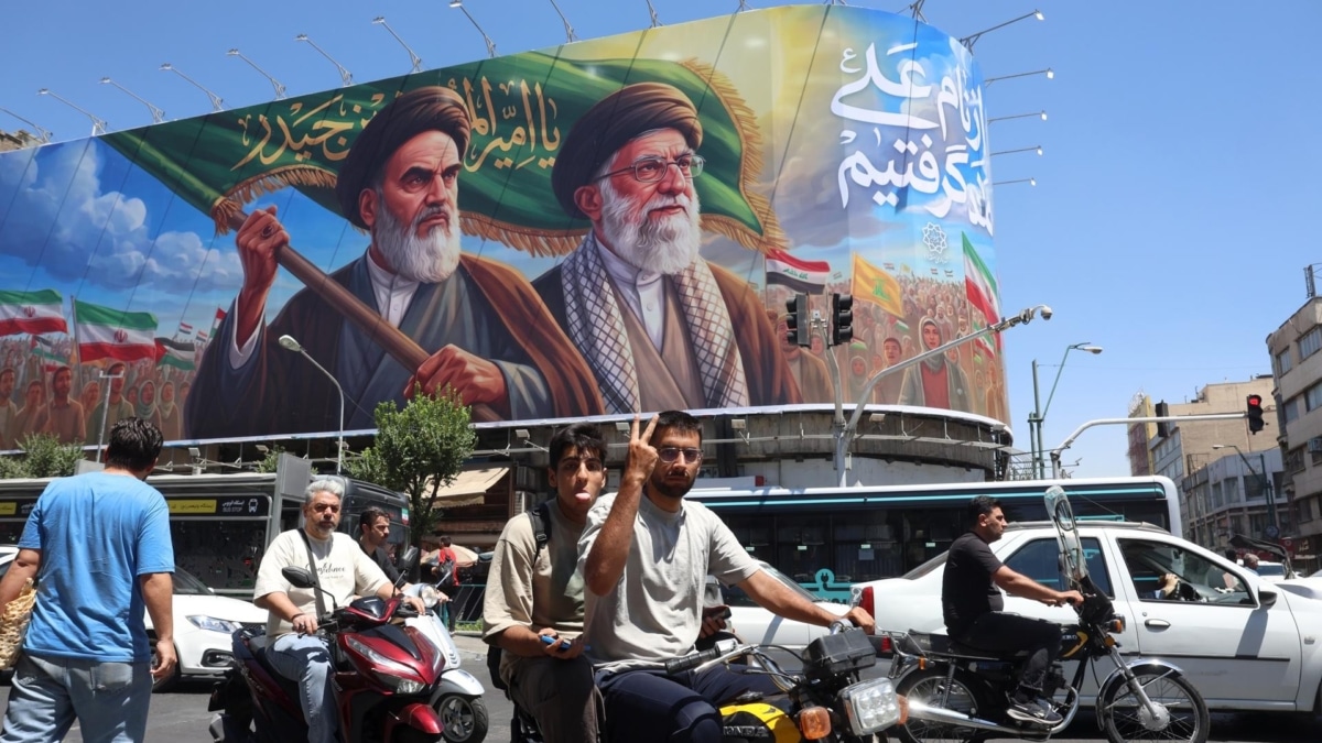 Un iraní muestra una señal de victoria mientras conduce junto a una valla publicitaria de los fallecidos líderes supremos iraníes, el ayatolá Ruhollah Khomeini y el ayatolá Ali Khamenei, en una calle de Teherán, Irán.