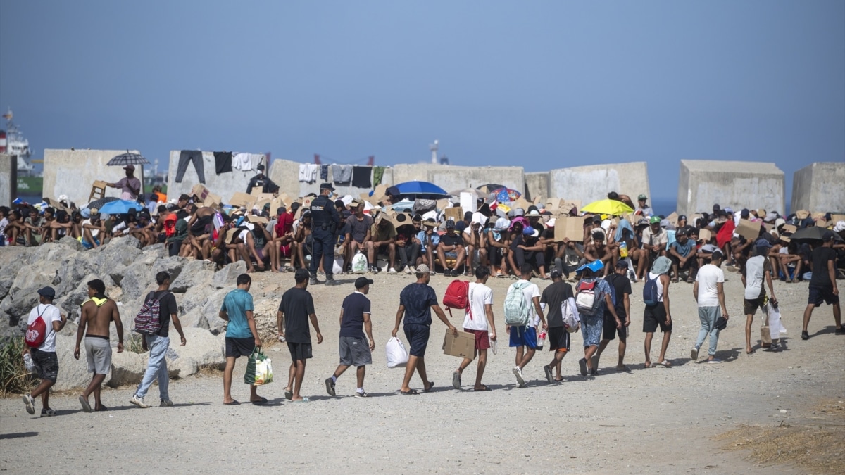 Decenas de migrantes caminan por la playa del Trampolín, a 31 de agosto de 2026, en Ceuta
